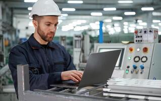 Using the, laptop. Factory worker is ,indoors with hard hat photo