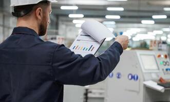 Turning ,,the, pages of documents. Factory worker is indoors with hard hat photo
