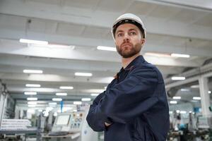 Posing,, with arms crossed. Factory worker is indoors with hard hat photo