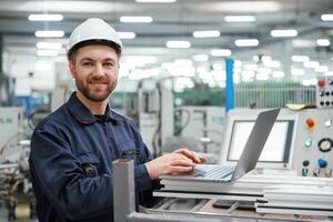 Using the laptop., Factory worker is indoors with hard hat photo