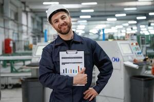 Happy, with ,results, holding graphs. Factory worker is indoors with hard hat photo