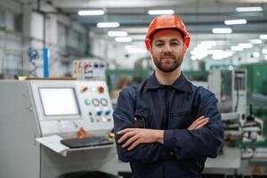 Standing, with arms crossed. Factory,, worker is indoors with hard hat photo