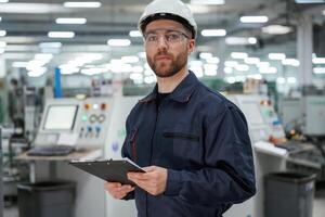 Looking, far, away, holding notepad. Factory worker is indoors with hard hat photo