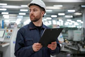 Looking far, away, holding notepad. Factory worker is indoors with hard hat photo