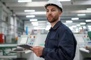 Looking far ,away, holding ,notepad. Factory worker is indoors with hard hat photo