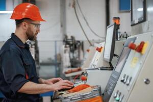 Side view, operating the machine. Factory worker is indoors with hard hat photo
