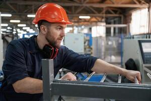 Working with machinery. Factory worker is indoors with hard hat photo