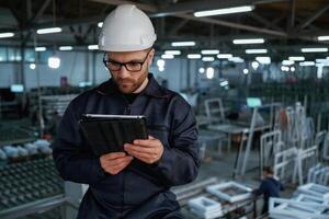 Reading the data from tablet. Factory worker is indoors with hard hat photo