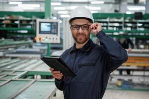 Machine behind, holding ,notepad. Factory worker is indoors with hard hat photo