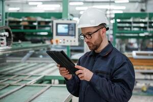 Machine, behind,, holding notepad. Factory worker is indoors with hard hat photo