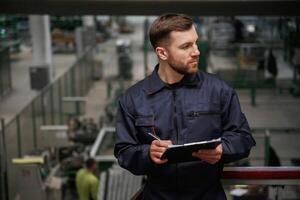 Writing ,,information into the notepad. Factory worker is indoors with hard hat photo