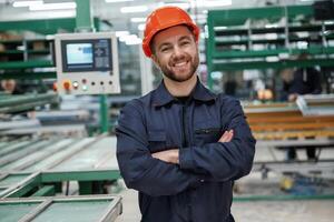 Beautiful man is, standing with arms crossed. Factory worker is indoors with hard hat photo