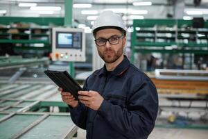 Machine, behind, holding notepad. Factory worker is indoors with hard hat photo