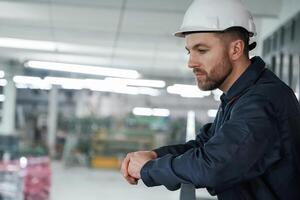 Leaning on the, railings. Factory worker is indoors with hard hat photo