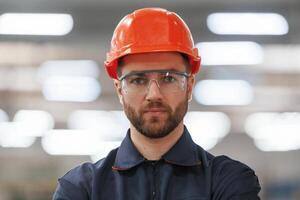 Focused, portrait, in glasses. Factory worker is indoors with hard hat photo