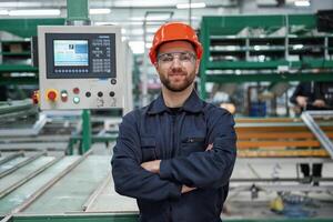 Beautiful, man is standing with arms crossed. Factory worker is indoors with hard hat photo