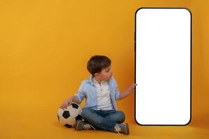 With huge ,smartphone, copy space, place. Little boy is in the studio against yellow background photo