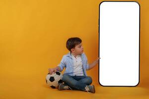 With, huge smartphone, copy space place. Little boy is in the studio against yellow background photo