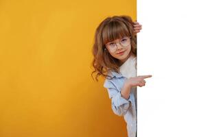 Hiding behind, yellow ,background for copy space. Cute little girl is in the studio photo