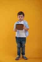 Tablet in hands. Little boy is in, the studio against yellow background photo
