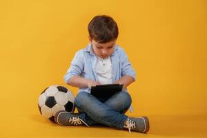 Table,t in hands. Little ,boy is in the studio against yellow background photo