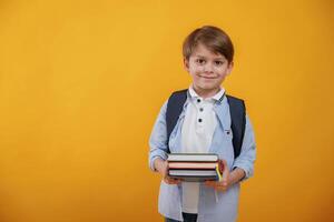 Ready for the school, holding ,books. Little boy is in the studio against yellow background photo