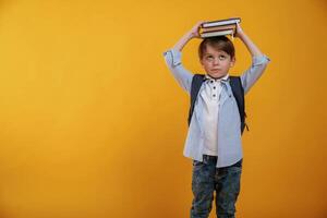 Playing ,with ,book, holding ,it on the head. Little boy is in the studio against yellow background photo