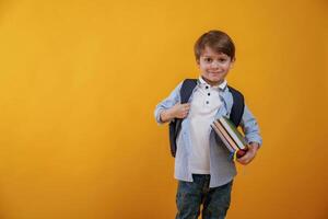 Ready for the, school, holding books. Little boy is in the studio against yellow background photo