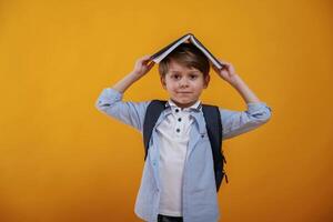 Playing ,,with book, holding it on the head. Little boy is in the studio against yellow background photo