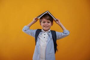 Book ,is ,above the head, having fun. Little boy is in the studio against yellow background photo