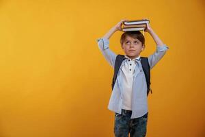 Playing ,with book, holding it on the head. Little boy is in the studio against yellow background photo