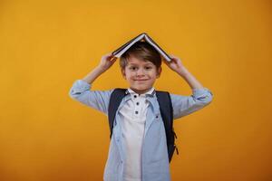 Playing, with book, holding, it on the head. Little boy is in the studio against yellow background photo