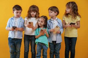 Using smartphones. Kids, are together against yellow background photo
