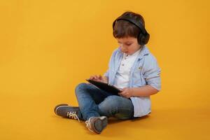 Tablet in, hands... Little boy is in the studio against yellow background photo