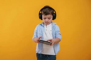 Tablet in, hands. Little boy is in the studio against yellow background photo