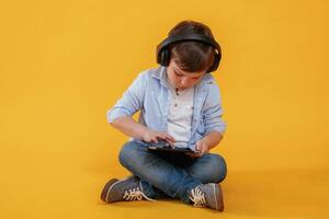 Tablet, in hands. Little boy is in the studio against yellow background photo