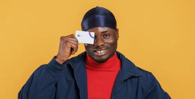 Covering eye by credit card. Handsome black man is in the studio against yellow background.. photo