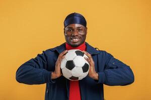Holding soccer,, ball. Handsome black man is in the studio against yellow background photo