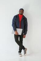 Standing and holding laptop in hand.., Black man in cap is in the studio against white background photo