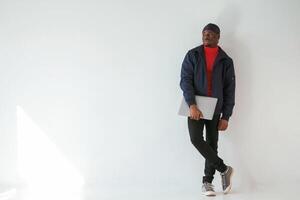 Standing and holding laptop, in, hand., Black man in cap is in the studio against white background photo