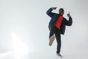 Showing ,,thumbs up, having fun. Black man in cap is in the studio against white background photo
