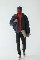 Silver colored laptop in hand., Black man in cap is in the studio against white background photo