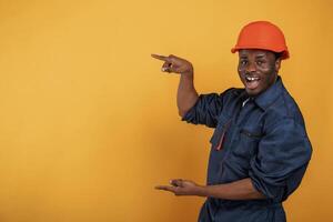 Guy in hard hat showing copy space by,, fingers. Handsome black man is in the studio against yellow background photo