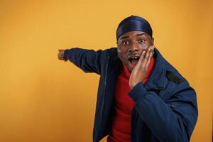 Shocked, showing ,,something by ,hand on the wall. Handsome black man is in the studio against yellow background photo