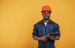 Digital, tablet in hand, construction, worker. Handsome black man is in the studio against yellow background photo