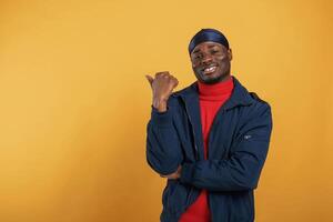 Showing something behind him by finger. Handsome black man is in the studio against yellow background photo