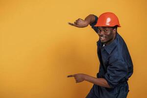 Guy in hard, hat, showing copy space by fingers. Handsome black man is in the studio against yellow background photo