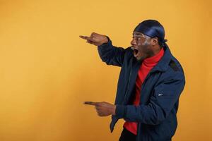 Shocked, showing ,something ,by hand on the wall. Handsome black man is in the studio against yellow background photo