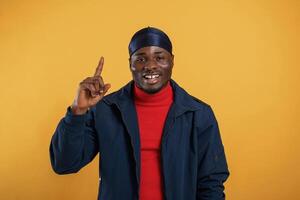 Pointing, by the finger to, copy space. Handsome black man is in the studio against yellow background photo