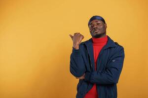 Showing something ,behind him by finger. Handsome black man is in the studio against yellow background photo